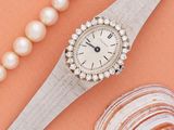 une image représentant une montre pour femme ornée de perles et d'un coquillage sur fond rose