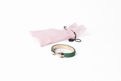 un bracelet vert et un sac rose posés sur une surface blanche