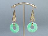 paire de boucles d'oreilles en jade vert et or, posées sur un support en métal