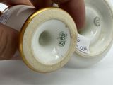 a hand that is holding a white vase with a gold rim