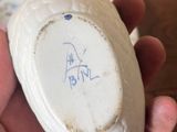 a hand holding a white porcelain object with a blue marker