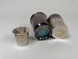 three silver shot glasses and a silver cup on a white surface