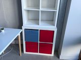 a white desk with a red and blue drawer next to a white bookcase