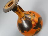 an orange vase with a black and gold design on it