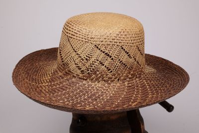 une image représentant un chapeau de paille posé sur un support en bois
