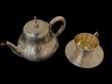 a silver tea pot and a silver cup on a black background