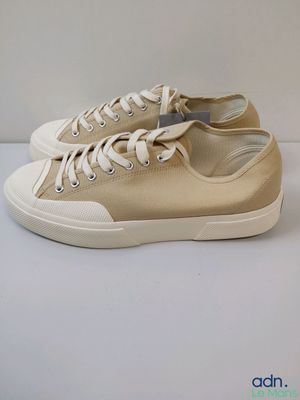 baskets en toile beige avec des lacets blancs sur un fond blanc
