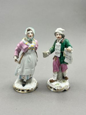 pair of porcelain figurines of a man and a woman holding a newspaper