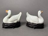 pair of white porcelain ducks on black bases on grey background