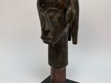 une sculpture en bois représentant la tête d'une femme, posée sur un socle noir