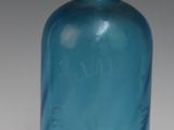 une bouteille en verre bleue avec un bouchon doré, posée sur une surface blanche