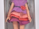 poupée dans une boîte, vêtue d'une robe rose et violette et d'un nœud rouge