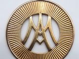 un pendentif en or représentant la lettre « m » dans un cercle, entouré de rayons