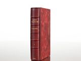 an old red book sitting on top of a table next to a white wall