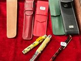 Plusieurs stylos et crayons sont posés dans un étui sur un tapis rouge.