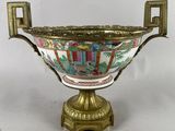 un vase richement décoré, posé sur un socle doré, sur fond blanc