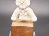 une image représentant une petite statue d'une personne assise sur un bloc de bois