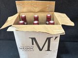 trois bouteilles de vin rouge dans une boîte en carton sur fond noir