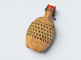 a small woven bottle with a red top on a white surface