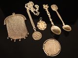 Plusieurs objets en argent sont exposés sur un fond noir, accompagnés d'une pièce de monnaie