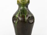 un vase vert et noir posé sur une surface blanche