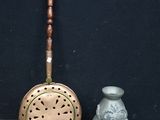 a small silver vase next to a metal strainer
