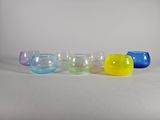 six bols en verre de couleurs différentes alignés les uns à côté des autres sur une surface blanche