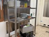 une étagère en acier inoxydable sur laquelle sont posés de la vaisselle et des casseroles, dans une cuisine