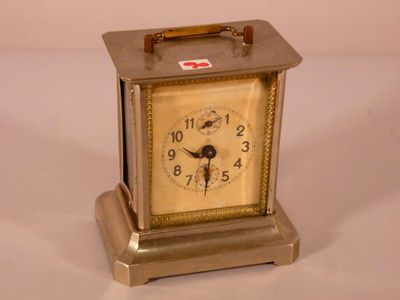 a small silver clock with a red cross on it