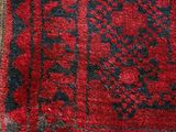 an old red and black rug with a black border on a wooden floor