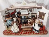 une maison de poupées miniature avec des poupées à l'intérieur, posée sur une table