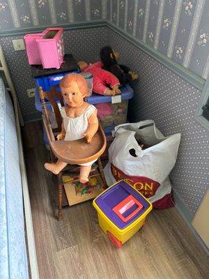 une poupée assise dans une chaise haute dans un coin de la pièce