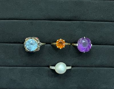 trois pierres précieuses de couleurs différentes et une bague avec une perle, posées sur un fond noir