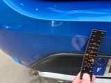 a person holding a ruler in front of a blue car