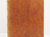 an old book with a brown cover sitting on a white surface