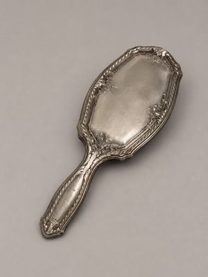 un miroir ancien plaqué argent, muni d'une poignée, sur un fond blanc
