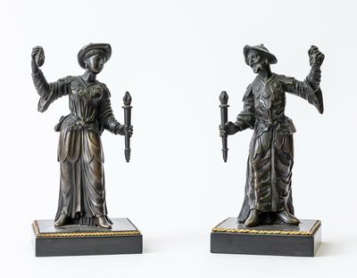 pair of antique bronze figurines of a woman holding a torch and a candle