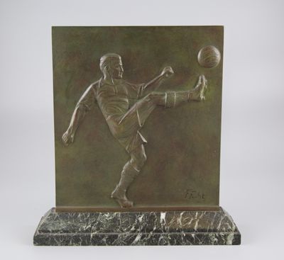 sculpture en bronze représentant un homme en train de frapper un ballon de football, posée sur un socle en marbre