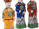 trois figurines chinoises représentant des hommes portant un chapeau et une queue-de-pie, sur fond blanc