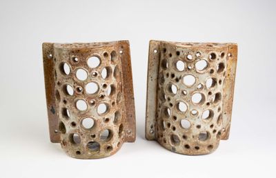 deux vases marron percés de trous, posés sur une surface blanche