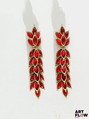 une paire de boucles d'oreilles rouges et dorées posées sur une surface blanche