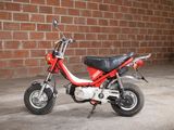 a small red motorcycle parked in front of a brick wall