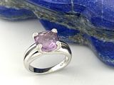 une photo d'une bague sertie d'un saphir rose et de diamants, posée sur un rocher