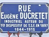un panneau bleu indiquant « rue Eugène Ducrett, industriel et inventeur du premier dispositif de se en 1897 »