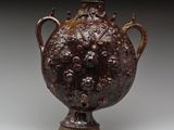 un vieux vase marron muni d'une anse et de poignées sur un fond gris