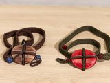 two bracelets with a red heart and a green cord on a wooden table