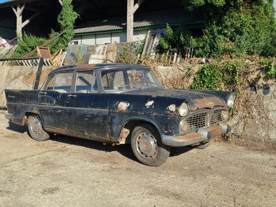 une vieille voiture rouillée garée devant un immeuble entouré d'une clôture en bois