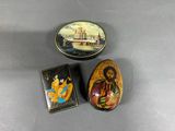 two small tins with paintings on them sitting on a table
