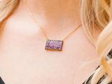 a woman wearing a necklace with a purple druzy stone on it