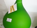 un vase vert posé sur une étagère blanche, à côté d'un verre